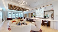 Located at 1601 Maguire Rd in Ocoee, Florida, this thoughtfully designed single-floor amenity space offers an expansive and cohesive layout that blends elegance with functionality. The reception and entrance areas set an immediate tone of refinement, featuring light hardwood flooring, glass partitions, a striking marble-clad feature wall, and sleek pendant lighting. A central lounge area serves as the heart of the space, distinguished by soaring ceilings with an intricate coffered wood grid, floor-to-ceiling windows that flood the room with natural light, and curated seating in a sophisticated palette of cream, burgundy, and teal. Adjacent to the main lounge is a cozy library-style nook with built-in wood shelving and curved banquette seating. The dining area offers a bright, airy setting with tall windows framing lush outdoor views. The game room is a standout feature, anchored by a custom billiards table beneath a dramatic coffered ceiling with statement pendant fixtures, complemented by wood-paneled walls, a large mounted television, and a dedicated bar-height workstation. The private office is a compact yet polished workspace equipped with a dual-monitor workstation, stylish art, and a modern chandelier. Throughout, the design maintains a cohesive contemporary aesthetic with warm wood tones, curated artwork, and high-end finishes.