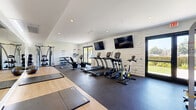 Located at 8501 S Sepulveda Blvd in Los Angeles, CA, this fitness center is a thoughtfully designed single-floor exercise facility offering a comprehensive workout environment. The space features a clean, modern aesthetic with white-painted shiplap accent walls, recessed lighting, and a combination of rubber flooring and hardwood-style flooring that delineates distinct workout zones.

The cardio section is outfitted with multiple True-brand treadmills and stationary bikes, all positioned beneath wall-mounted flat-screen TVs for entertainment during workouts. A dedicated strength training area includes a multi-function cable machine, adjustable weight bench, and a tiered dumbbell rack, providing ample options for resistance training. Medicine balls and stability balls are neatly organized on dedicated racks along the perimeter.

A spacious stretching and functional fitness zone features hardwood-style flooring, foldable exercise mats, and foam rollers, offering a clean and open area for floor exercises and flexibility work. A full-length mirror wall visually expands the space and provides form feedback during training.

Large black-framed glass doors on two walls flood the interior with natural light and open to outdoor greenery, creating an airy, inviting atmosphere. A water cooler station ensures hydration convenience. The overall design balances functionality and comfort, making this fitness center a well-rounded facility for all workout needs.