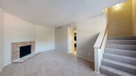 This two-story home in Austin, TX offers three bedrooms and three bathrooms across two well-proportioned floors. The main level opens with a carpeted living room highlighted by a classic brick fireplace, a staircase with white-painted balustrades, and a window that brings in natural light near the entryway. The kitchen is thoughtfully appointed with rich dark wood cabinetry, a mosaic tile backsplash, granite-style countertops, and a full suite of black appliances including a range, microwave, dishwasher, and refrigerator, all set on wood-look flooring. The upper floor houses the bedrooms, connected by a carpeted hallway. The primary bedroom includes a walk-in closet with built-in shelving. The bathrooms feature dark wood vanities, granite countertops, wood-look flooring, and framed mirrors. One bathroom showcases a uniquely angled ceiling, adding architectural character. Throughout the home, textured ceilings, neutral wall tones, and consistent finishes create a cohesive and comfortable ambiance. Two closets provide ample storage, complementing the functional layout of this well-designed Austin home.