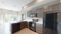 Located at 3080 E Cherry St in Springfield, MO, this two-bedroom, two-bathroom residence offers a thoughtfully designed single-level layout. The open-concept kitchen is a standout feature, showcasing rich dark espresso cabinetry, light quartz-style countertops, and a full suite of black Whirlpool appliances including a range, microwave, dishwasher, and refrigerator. Light wood-style flooring runs throughout the main living and kitchen areas, complementing the neutral gray tones of the walls and creating a clean, modern aesthetic. A large window in the kitchen area allows natural light to flow into the adjacent living space. The entry area features durable wood-style flooring and charcoal-toned doors that carry through the unit's cohesive design language. Both bedrooms are carpeted and offer windows with outdoor views, providing a quiet and comfortable retreat. The primary bedroom includes direct access to a closet and bathroom. Each bathroom is finished with dark wood vanities, marble-patterned countertops, large mirrors, and modern brushed nickel fixtures. The unit also includes a dedicated laundry area and a utility room, adding practical functionality to the space.