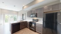 Located at 3080 E Cherry St in Springfield, MO, this two-bedroom, two-bathroom residence offers a thoughtfully designed single-level layout. The open-concept kitchen is a standout feature, showcasing rich dark espresso cabinetry, light quartz-style countertops, and a full suite of black Whirlpool appliances including a range, microwave, dishwasher, and refrigerator. Light wood-style flooring runs throughout the main living and kitchen areas, complementing the neutral gray tones of the walls and creating a clean, modern aesthetic. A large window in the kitchen area allows natural light to flow into the adjacent living space. The entry area features durable wood-style flooring and charcoal-toned doors that carry through the unit's cohesive design language. Both bedrooms are carpeted and offer windows with outdoor views, providing a quiet and comfortable retreat. The primary bedroom includes direct access to a closet and bathroom. Each bathroom is finished with dark wood vanities, marble-patterned countertops, large mirrors, and modern brushed nickel fixtures. The unit also includes a dedicated laundry area and a utility room, adding practical functionality to the space.