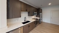 Located at 1449 S Church St in Charlotte's South End neighborhood, this single-floor unit offers a thoughtfully designed layout with modern finishes throughout. Light wood-look flooring flows seamlessly across the open-concept living and kitchen areas, creating a cohesive and airy feel.

The kitchen is a standout feature, showcasing rich dark wood cabinetry extending floor to ceiling for ample storage, complemented by crisp white quartz countertops and a striking geometric white tile backsplash. A matte black undermount sink, stainless steel appliances—including a French door refrigerator, electric range, built-in microwave, and dishwasher—complete this well-appointed space.

The open living area benefits from natural light through a window and connects effortlessly to the kitchen, making it ideal for everyday living and entertaining. The bedroom is bright and comfortable, featuring windows with views of greenery, a ceiling fan with light fixture, and access to a spacious walk-in closet outfitted with wire shelving along two walls for generous storage.

The bathroom is clean and functional, featuring a tiled tub-and-shower combination with warm earth-tone tile surround, a white soaking tub, quartz vanity countertop, and wood-toned cabinetry. The overall design of the unit blends contemporary aesthetics with practical, well-considered details throughout.