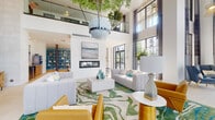 Located at 9491–9499 SW 174th St in Palmetto Bay, Florida, this single-floor amenity space is defined by its dramatic double-height ceilings and expansive floor-to-ceiling windows framed in dark steel, flooding the interior with abundant natural light and views of the surrounding landscape. Large-format porcelain tile flooring anchors the grand entrance lobby, where a suspended oversized planter with a live tree serves as a striking architectural focal point overhead.

The main lounge area features plush modular seating in neutral tones and cognac leather, arranged atop a vivid swirling green-and-blue area rug that evokes a coastal aesthetic. A sleek linear fireplace set against a textured wave-pattern stone accent wall adds warmth and visual interest. An integrated work bar with warm wood cabinetry and counter seating provides a functional co-working zone adjacent to a glass-enclosed workspace.

A secondary lounge area transitions to light hardwood flooring and includes comfortable seating, a wall-mounted TV, bold teal built-in bookshelves, and a linear fireplace with direct pool-view access. A dedicated refreshment station with warm wood cabinetry, beverage equipment, and curated artwork completes the space, contributing to an overall ambiance that is polished, resort-inspired, and highly livable.