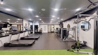 Located at 84 Washington Ave in Belleville, NJ, this fitness center offers a thoughtfully designed exercise space spread across a single floor. The room is finished with a combination of durable grey flooring and a vibrant artificial turf zone, clearly delineating cardio and functional training areas. Recessed ceiling lighting throughout ensures consistent, bright illumination across the entire space.

The cardio section features multiple treadmills and a stationary spin bike, complemented by large wall-mounted mirrors that enhance the sense of openness. The strength training area is anchored by a Life Fitness cable machine and a multi-functional power rack, along with a selection of benches, selectorized resistance machines, and free weights. Battle ropes are mounted along the ceiling, adding a functional fitness element to the space.

Motivational typography is displayed across the white walls, contributing to an energizing atmosphere. A green living wall accent panel and wall-mounted flat-screen televisions add visual interest to the training area. A water fountain is also available within the space for convenience. The overall design balances a modern, clean aesthetic with a performance-focused environment, making it a comprehensive facility for a full range of workout routines.