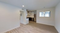 This 2-bedroom, 1-bathroom residence is thoughtfully designed to maximize functionality and comfort within a single-floor layout. The open-concept living and kitchen area creates a seamless flow, making the space feel bright and welcoming. Light-toned wood-style flooring runs throughout the main living area, complementing the clean, white walls and recessed lighting that keep the interior feeling fresh and modern. The kitchen features white upper cabinetry, dark lower cabinetry, a subway tile backsplash, and stainless steel appliances, including a refrigerator and dishwasher. A pendant light fixture adds a stylish focal point above the kitchen space. A window in the adjoining dining or living area allows natural light to filter in, enhancing the airy ambiance. The transition from the living area to the hallway is defined by a structural column, leading toward the bedrooms and bathroom. A utility panel is conveniently accessible near the hallway entry. The overall aesthetic is clean and contemporary, with a neutral color palette that provides a versatile backdrop for a variety of interior styles. This unit offers a practical and modern living experience with well-chosen finishes throughout.