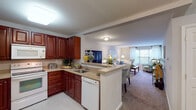 This thoughtfully designed single-floor residence offers a comfortable and functional layout with a seamless flow between its living spaces. The open-concept kitchen connects directly to the living area, creating an inviting, connected environment. The kitchen is outfitted with rich cherry wood cabinetry, granite-style countertops, white appliances including a range, built-in microwave, and dishwasher, along with a peninsula that serves as both a workspace and casual dining area. Tile flooring completes the kitchen's clean, practical aesthetic.

The living room is bright and welcoming, with plush carpeting, large windows that invite natural light and offer pleasant outdoor views of surrounding greenery, and ample space for comfortable seating arrangements. A wall-mounted television adds a modern touch to the dining and living areas.

The primary bedroom is generously sized, featuring carpet flooring, large windows with decorative drapery, and room for substantial furniture. Its en-suite bathroom includes a single vanity, tiled shower, and tile flooring. The second bedroom is equally comfortable, with natural light from an outdoor-facing window. A second full bathroom with a soaking tub and shower combination serves this area. The overall ambiance is warm, neutral, and move-in ready.