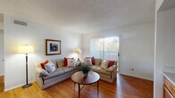 This single-floor residence offers a functional and comfortable layout across several distinct living areas. The living room serves as the heart of the space, featuring warm hardwood-style flooring, a textured ceiling, and a large sliding glass door fitted with vertical blinds that allows generous natural light and provides access to an outdoor area with views of surrounding greenery.

Adjacent to the living room, a dedicated dining area accommodates a four-seat table and benefits from the same flooring, creating a cohesive flow between spaces. Framed artwork on the walls adds a decorative touch throughout.

The galley-style kitchen is efficiently designed with abundant warm-toned wood cabinetry lining both sides, light-colored countertops, and hardwood-style flooring. It is equipped with black and stainless steel appliances, including a range, microwave, refrigerator, and dishwasher. A pantry closet provides additional storage within the kitchen corridor.

The bedroom is carpeted for comfort and features a ceiling fan with light fixture, natural light from a window with blinds and curtain panels, and ample room for furnishings. The full bathroom includes a tub-shower combination with tile surround, a wood-cabinet vanity with stone-look countertop, and hardwood-style flooring, completing this well-organized residence.