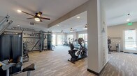 This expansive single-floor fitness center is thoughtfully designed to support a full range of workout disciplines. The space is divided into distinct functional zones, each tailored to a specific type of training. The cardio area features multiple treadmills, ellipticals, and stationary bikes positioned along large windows that invite generous natural light and outdoor views, creating an energizing atmosphere for endurance training. Ceiling fans throughout maintain comfort across all areas of the facility.

A dedicated strength training zone houses an extensive dumbbell rack, kettlebells in varied weights, adjustable benches, and weight machines, all set on durable rubberized flooring. Full-length mirrors line the walls to support proper form and enhance the sense of space. A standout feature of the facility is the textured climbing wall, adding a dynamic and unique element rarely found in standard fitness centers.

Motivational quotes and large-scale photographic murals — including a vivid coastal sunset scene — are integrated throughout the walls, reinforcing an upbeat, goal-oriented atmosphere. The neutral gray and white color palette keeps the space feeling clean and modern. Additional equipment including a smith machine, cable machines, and stability balls ensures comprehensive training options, making this fitness center a versatile and well-appointed facility.