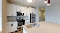 Located at 223 E Town St in the heart of Columbus, Ohio, this modern single-floor residence offers a thoughtfully designed living space with clean, contemporary finishes throughout. The kitchen stands as a centerpiece of the home, showcasing crisp white shaker-style cabinetry that reaches toward the ceiling for ample storage. Stainless steel appliances — including a French door refrigerator, electric range with oven, and over-the-range microwave — lend a polished, professional feel to the space. A generously sized island with a light quartz countertop and an undermount stainless steel sink serves as both a functional workspace and a natural gathering point. Recessed lighting and flush-mount ceiling fixtures ensure the kitchen remains bright and welcoming. The open layout connects the kitchen seamlessly to adjacent living areas, creating an easy flow throughout the home. Warm wood-tone flooring anchors the space, complementing the neutral color palette of soft whites and greiges that runs throughout. The overall ambiance is clean, modern, and move-in ready, making it an ideal home for those seeking contemporary urban living in downtown Columbus.