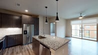 This well-appointed 2-bedroom, 2-bathroom residence offers a thoughtfully designed single-level floor plan with modern finishes throughout. The open-concept kitchen serves as the heart of the home, anchored by a large granite-topped island with an undermount sink and dramatic pendant lighting overhead. Dark espresso cabinetry contrasts beautifully with the light granite surfaces, while stainless steel appliances — including a French door refrigerator, range, microwave, and dishwasher — complete the sleek look. A white subway tile backsplash adds a clean, contemporary touch. Wood-style flooring flows through the kitchen and living areas, leading to a generous living room equipped with a ceiling fan and a sliding glass door that invites natural light and outdoor views. Both bedrooms feature soft carpeting and windows with blinds. The primary bathroom impresses with a dual-sink granite vanity, dark cabinetry, wood-style flooring, and a glass-enclosed tiled shower. The second bathroom mirrors this refined aesthetic with its own dual-sink granite vanity and a tub-shower combination. Neutral wall tones throughout lend a clean, move-in-ready ambiance to this modern residence.