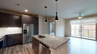 This well-appointed 2-bedroom, 2-bathroom residence offers a thoughtfully designed single-level floor plan with modern finishes throughout. The open-concept kitchen serves as the heart of the home, anchored by a large granite-topped island with an undermount sink and dramatic pendant lighting overhead. Dark espresso cabinetry contrasts beautifully with the light granite surfaces, while stainless steel appliances — including a French door refrigerator, range, microwave, and dishwasher — complete the sleek look. A white subway tile backsplash adds a clean, contemporary touch. Wood-style flooring flows through the kitchen and living areas, leading to a generous living room equipped with a ceiling fan and a sliding glass door that invites natural light and outdoor views. Both bedrooms feature soft carpeting and windows with blinds. The primary bathroom impresses with a dual-sink granite vanity, dark cabinetry, wood-style flooring, and a glass-enclosed tiled shower. The second bathroom mirrors this refined aesthetic with its own dual-sink granite vanity and a tub-shower combination. Neutral wall tones throughout lend a clean, move-in-ready ambiance to this modern residence.