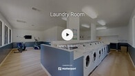 Located at 1500 Shadowridge Drive Southeast in Vista, CA, this single-floor community amenity facility combines a full-service laundry room with a dedicated fitness area in one efficiently designed space. The interior features a clean, modern aesthetic with a two-tone color scheme of crisp white upper walls and slate blue lower panels, complemented by light wood-style flooring throughout.

The laundry area is the centerpiece of the space, equipped with a generous row of front-load washing machines and dryers arranged along a central island and perimeter walls. A white laminate countertop surface spans the machine island, providing practical folding space. Overhead, bright flush-mount and recessed lighting ensures excellent visibility throughout the room.

A dedicated fitness alcove occupies one section of the facility, furnished with a recumbent exercise bike and an elliptical trainer, along with a wall-mounted flat-screen television — an ideal setup for staying active. Large windows line one wall of this area, flooding the space with natural light and offering pleasant views of an outdoor playground and surrounding greenery.

The facility's open floor plan promotes easy circulation, while the ample square footage accommodates multiple users simultaneously. Overall, the space delivers a functional, well-maintained environment designed to serve the everyday needs of a residential community.