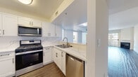 This single-story residence in the 94597 zip code of California offers a thoughtfully updated interior with a clean, modern aesthetic throughout. The kitchen is a standout feature, showcasing white shaker cabinetry with matte black hardware, quartz countertops with striking veined marbling, and a matching backsplash. Stainless steel appliances—including a gas range, built-in microwave, dishwasher, and refrigerator—complete the space, which opens toward the main living area via a pass-through layout.

The living area is generously sized, featuring wood-look plank flooring in a warm gray tone, crisp white walls, and recessed lighting. The open flow connects the kitchen and living spaces seamlessly, creating an inviting, functional layout.

The bedrooms are finished with plush neutral carpeting and feature mirrored sliding closet doors that enhance the sense of space. Each room is well-proportioned with ample natural light.

Both bathrooms are updated with white shaker vanities, brushed nickel fixtures, and tub-shower combinations enclosed by sliding glass doors. One bathroom features wood-look tile flooring, while the other continues the warm hardwood-style planks found in the kitchen. The overall ambiance is bright, clean, and move-in ready.