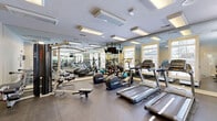 Located at 1660 Hampton Knoll Drive in Akron, Ohio, this fitness center offers a well-appointed, single-floor layout comprising two dedicated exercise rooms. The space is generously sized, providing ample room for a diverse range of workout activities without feeling cramped.

The exercise rooms are outfitted with a strong selection of cardio equipment, including multiple Matrix-brand treadmills and elliptical machines, as well as a rowing machine. Strength training is well represented with a multi-station cable machine, a free weights rack stocked with a variety of dumbbells, and a flat workout bench. A stability ball adds flexibility training options to the mix.

Floor-to-ceiling mirrored walls run along multiple sides of the rooms, visually expanding the space and supporting proper form during exercise. The flooring is durable, dark rubberized gym matting, practical and easy to maintain. Recessed fluorescent panel lighting illuminates the space evenly throughout.

Windows along one wall allow natural light to filter in, enhancing the open and airy atmosphere. A wall-mounted television provides entertainment during workouts. Informational fitness posters and a hand sanitizing station reflect a thoughtful, user-focused design. The overall ambiance is clean, functional, and well-maintained, making this fitness center a capable and inviting facility for residents.