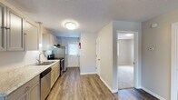 Located at 1600 Arlington Blvd in Greenville, NC, this single-floor unit offers a clean, updated interior designed for comfortable everyday living. The open living area is finished with durable wood-look plank flooring and features a ceiling fan with light fixture, providing both functionality and a welcoming ambiance. Textured ceilings and neutral wall tones carry throughout, creating a cohesive and bright aesthetic.

The kitchen is well-appointed with gray cabinetry, light granite-style countertops, a stainless steel sink, and stainless steel appliances including an electric range and refrigerator. A range hood is installed above the stove, and a door at the end of the kitchen provides direct exterior access, allowing natural light to filter in through its window.

Adjacent to the main living space, the bedroom features plush carpeting and a generously sized closet with double doors and a full-width hanging rod, offering ample storage. The bathroom is equipped with a full-size soaking tub and shower combo with a clean white surround.

A central hallway connects the key areas of the unit, with a louvered closet door providing additional storage. The overall layout is efficiently designed, making practical use of the available space while maintaining an open and airy feel throughout.