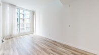 Located at 2061 Rue Stanley in the heart of downtown Montréal, this thoughtfully designed one-bedroom, one-bathroom unit offers a compact yet highly functional layout across a single floor. Light hardwood flooring flows throughout, creating a warm, cohesive aesthetic that ties each area together seamlessly.

The open-concept living and kitchen area forms the heart of the unit. The kitchen is outfitted with white cabinetry reaching toward the ceiling, a dark granite countertop with under-cabinet accent lighting, a black tile backsplash, a stainless steel range with oven, a dishwasher, and a microwave. A large window with sheer curtains floods the living space with natural light and provides views of the surrounding urban cityscape.

The bedroom is efficiently designed with a built-in platform bed base, an integrated desk surface, wall-mounted open shelving for storage, and floor-to-ceiling windows that frame city views and bring in abundant daylight. An exposed concrete accent column adds an industrial touch to the otherwise clean, minimalist aesthetic.

The bathroom features large-format light tile throughout, a glass-enclosed walk-in shower with a rain showerhead, a wall-mounted toilet, and a floating vanity topped with a dark granite counter and an undermount sink. Built-in shelving above the vanity provides additional storage. A dedicated closet and hallway complete this well-appointed urban residence.