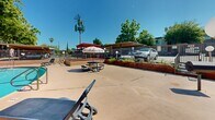 Located on Fair Oaks Boulevard in Carmichael, California, this outdoor communal amenity area serves as a central gathering and recreation space. The centerpiece is a generously sized swimming pool with clear, inviting blue water, accessible via built-in entry steps and handrails. A second, kidney-shaped pool is also present, offering additional aquatic options within the same fenced enclosure.

The surrounding pool deck provides ample space for lounging, with multiple reclining chairs and chaise lounges positioned to take advantage of the abundant California sunshine. A shaded pergola structure finished in red adds a vibrant accent to the space and offers a covered retreat from the sun. Additional covered parking or shade structures are visible along the perimeter, providing practical utility alongside the recreational features.

A dedicated patio area with a tile-top table and seating, along with a BBQ grill, creates an ideal outdoor dining and entertaining zone, bordered by mature hedges and ornamental iron fencing that offer both privacy and greenery. Globe-style light fixtures are positioned throughout, suggesting the space is well-lit for evening use.

Mature trees frame the area, softening the hardscape and contributing to a pleasant, park-like atmosphere. The overall layout is well-organized and well-maintained, making it a functional and appealing outdoor amenity for residents of the surrounding community.