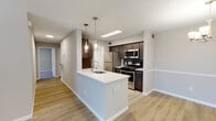 This two-story residence at Avalon Gardens offers a well-designed 2-bedroom, 1-bathroom layout with a bonus loft, combining modern finishes with functional living spaces across two levels. The main level features an open-concept living and dining area with light hardwood-style flooring and a chandelier overhead. The kitchen is equipped with dark espresso cabinetry, a blue tile backsplash, stainless steel appliances including a gas range, microwave, and refrigerator, and a peninsula with a white countertop and pendant lighting — ideal for casual dining and meal prep. The dining area flows naturally from the kitchen, creating a cohesive, airy entertaining space. The full bathroom is appointed with marble-style tile walls, a white shaker-style vanity with brushed nickel hardware, a mirrored medicine cabinet, and a tub-shower combination. Both bedrooms are carpeted and offer closet storage, with one bedroom featuring a window with natural views of mature trees. A dedicated in-unit laundry space houses a front-loading washer. The upper loft level provides additional flexible living space with carpeting and built-in shelving, making it ideal as a home office, study, or additional lounge area. Neutral wall tones and textured ceilings are consistent throughout the home.