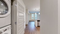 Located on the fifth floor in Bellevue, WA, this contemporary unit features a clean, modern design with wood-look flooring throughout the main living areas and plush carpet in the bedrooms. The open-concept kitchen serves as a central highlight, showcasing white cabinetry extending to the ceiling, a white subway tile backsplash, a distinctive light-blue island with a dark countertop, and a full suite of stainless steel appliances including a refrigerator, range, microwave, and dishwasher. Pendant lighting above the island adds a refined finishing touch. The living and dining areas benefit from natural light streaming through generously sized windows that frame views of the surrounding Bellevue skyline. The bedrooms are carpeted and equally well-lit, each featuring large windows with urban views and baseboard heating. One bedroom includes a wall-mounted mini-split unit for additional climate control. The bathroom is finished with wood-look flooring, white cabinetry with dark countertops, a soaking tub, and direct access to a spacious walk-in closet outfitted with wire shelving and hanging rods. An in-unit washer and dryer are also included.