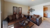 This single-floor residence offers a thoughtfully organized layout across several distinct living areas. The living room serves as the heart of the home, featuring plush carpeting, neutral warm-toned walls, and a large sliding glass door with vertical blinds that invites abundant natural light and outdoor views. The kitchen is outfitted with ample honey-toned wood cabinetry, generous counter space, a double sink, a dishwasher, and a refrigerator, all set atop durable tile flooring. Adjacent to the kitchen, the dining area provides an intimate setting with the same tile flooring and a cozy atmosphere. The primary bedroom is a serene retreat with carpeted floors, a window dressed with blinds and curtain panels, and comfortable proportions. A second bedroom carries a vibrant, colorful character with soft carpet and decorative wall accents. Both bathrooms are finished with tile flooring and warm wood vanities; one features a full bathtub and shower combination, while the other includes a walk-in shower. Throughout the residence, a consistent design language of warm neutrals, decorative wall art, and coordinated furnishings creates an inviting and cohesive ambiance.