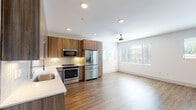 This two-story residence showcases a clean, modern design throughout. The open-concept main living area seamlessly connects the kitchen and living space, with warm hardwood-style flooring and recessed lighting overhead. A ceiling fan adds comfort to the living area, which receives generous natural light through large windows fitted with horizontal blinds.

The kitchen is a standout feature, offering two distinct configurations across the floors. Both kitchens are equipped with full stainless steel appliance suites, including a French door refrigerator, electric range, built-in microwave, and dishwasher. Warm wood-tone cabinetry extends to the ceiling, complemented by a textured tile backsplash and light quartz countertops.

The bathrooms reflect the same contemporary aesthetic. One features a glass-enclosed walk-in shower with white subway tile and brushed nickel fixtures, paired with a wood-tone vanity and lighted mirror. A second bathroom offers a full soaking tub with a tiled surround, a matching vanity, and tile flooring.

The bedrooms are carpeted and bright, with large windows offering outdoor views and ample natural light. A staircase connects the two floors, completing this well-designed and cohesive living space.