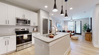 This well-designed single-floor residence showcases a cohesive modern aesthetic with light wood-style flooring and a neutral color palette throughout the main living areas. The open-concept kitchen is a standout feature, equipped with stainless steel appliances including a range, microwave, and refrigerator, complemented by white shaker cabinetry, a subway tile backsplash, and light quartz countertops. A central island with an undermount sink and three striking matte black pendant lights serves as the visual focal point, providing both workspace and casual seating potential.

The kitchen flows seamlessly into the living area, which benefits from natural light through large windows and features a ceiling fan overhead. Recessed lighting throughout the open-plan space ensures consistent illumination. The bedroom offers plush carpeting, a ceiling fan, and generous window coverage that allows ample natural light.

The bathroom is finished with a long dual-sink vanity, light quartz countertops, black hardware accents, wood-look tile flooring, and a tiled walk-in shower. A dedicated laundry area houses a stacked full-size washer and dryer unit alongside wire shelving for added storage, completing this thoughtfully appointed residence.
