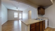 Located at 3435 E Southcross Blvd in San Antonio, Texas, this single-story unit offers a well-designed, functional layout highlighted by warm wood-look flooring that runs consistently throughout every room. The living area is bright and open, benefiting from natural light through a front-facing window and a glass-paneled exterior door, with a ceiling fan overhead adding comfort. A distinctive arched passageway connects the living space to the kitchen, lending architectural character to the interior. The kitchen is well-appointed with rich dark wood cabinetry, light granite-style countertops, a double-basin sink, a full suite of white appliances including a refrigerator, electric range, microwave, and dishwasher, and pendant lighting above the counter area. A peninsula-style counter provides additional prep space and an open sightline into the living area. The bathrooms feature matching dark wood vanities with granite-style countertops, large mirrors, and a tub-shower combination with white tile surround. Bedrooms are comfortably sized with neutral walls and ample natural light. A dedicated laundry room includes washer and dryer hookups, overhead wire shelving, and an electrical panel. The arched detailing and consistent finishes throughout create a cohesive and inviting atmosphere.