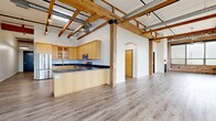 This industrial-style loft at 69 Cascade Dr in Rochester, NY, blends historic character with modern finishes across a generously sized single floor. The open-plan living and dining area is defined by soaring ceilings with exposed wooden timber beams, industrial ductwork, and walls of large windows framed by original brick columns that flood the space with natural light and offer views of the surrounding neighborhood. Light hardwood flooring runs throughout, complementing the warm tones of the brick and wood.

The well-appointed kitchen features warm maple cabinetry, dark granite countertops, stainless steel appliances including a gas range, microwave, dishwasher, and refrigerator, along with a central peninsula ideal for casual dining. A dedicated dining room sits adjacent to the kitchen, while the living room benefits from dramatic pendant lighting and expansive window banks.

The spacious primary bedroom includes exposed beam ceilings, brick accent walls, large windows, a ceiling fan, and ample closet space. The second bedroom is equally well-sized with beam ceilings and multiple closets. The full bathroom is finished with classic penny tile flooring, a soaking tub, a separate glass-enclosed shower, and built-in cabinetry. A dedicated laundry area and multiple hallways complete this distinctive urban loft.