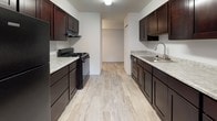Located at 3400 Eastern Blvd in York, Pennsylvania, this single-floor unit offers a clean, functional layout designed for comfortable everyday living. The open living area is finished with neutral wall-to-wall carpeting and features a sliding glass door with vertical blinds that floods the space with natural light while providing access to outdoor greenery views. The galley-style kitchen is well-appointed with rich dark cabinetry, light granite-style countertops, light wood-look tile flooring, and black appliances including a gas range and dishwasher, along with a stainless steel sink. Multiple bedrooms are carpeted and bathed in natural light from well-placed windows. The primary bedroom includes a walk-in closet with built-in shelving and rod, while a secondary bedroom features a sliding panel closet door, offering ample storage. An additional carpeted room provides flexible space for various uses. The unit includes two bathrooms: a full bath with a vanity, framed mirror, and tub-shower combination, and a second bath with a stall shower and stone-look tile flooring. Throughout, the unit maintains a bright, neutral palette with white walls and clean finishes, creating a light and welcoming atmosphere.