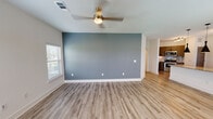This well-appointed single-floor residence showcases a clean, modern design with wood-look luxury vinyl plank flooring running consistently throughout every room, creating a cohesive and contemporary aesthetic. The open-concept living area is anchored by a striking slate-blue accent wall and a gold-tone ceiling fan, with natural light streaming in through multiple windows fitted with blinds. The space flows seamlessly into the kitchen, which is a functional standout featuring sleek gray cabinetry with matte black hardware, polished granite countertops, a large center island with pendant lighting, and a full suite of stainless steel appliances including an electric range, microwave, and refrigerator. The bedrooms are generously sized, each offering ceiling fans, natural light, and neutral gray accent walls for a calm, restful atmosphere. One bedroom includes access to a walk-in closet. The home features two bathrooms, each finished with granite-topped vanities, gray cabinetry, and marble-look tile. One bathroom offers a tub-shower combo, while the other includes a glass-enclosed walk-in shower. Track lighting and recessed fixtures add to the bright, modern feel throughout the home, making this a thoughtfully designed and move-in-ready space.