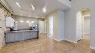 This two-story space showcases a thoughtfully designed open-concept layout that seamlessly connects the kitchen and living areas. The polished concrete floors throughout the main level add a sleek, contemporary feel while remaining highly durable and easy to maintain. Neutral beige and light gray tones on the walls create a clean, inviting atmosphere that complements the modern finishes.

The kitchen is a standout feature, equipped with a large center island clad in wood-toned cabinetry and topped with a stone-look countertop. White upper cabinets line the perimeter, offering ample storage, while stainless steel appliances, including a refrigerator with an ice and water dispenser, add a polished touch. A trio of pendant lights hangs above the island, providing focused task lighting alongside recessed ceiling fixtures that illuminate the space evenly.

The open layout extends toward a entry area with an arched doorway detail, contributing architectural interest. Tall ceilings amplify the sense of volume and airiness throughout the main floor. A second story adds additional living space above, making this a versatile and well-appointed multi-level property.
