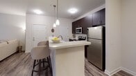 Located at 1710 Eighth Street Dr NE in Hickory, North Carolina, this single-floor residence offers a thoughtfully designed layout with a clean, contemporary aesthetic throughout. The kitchen is a standout feature, showcasing rich dark-espresso cabinetry that extends to the ceiling for ample storage, bright white quartz countertops, and a full suite of stainless steel appliances including an electric range, over-the-range microwave, and refrigerator. A peninsula with pendant lighting and bar seating connects the kitchen to the main living area, creating an open and functional flow ideal for both everyday living and entertaining. The living area is finished with wood-look plank flooring that carries through much of the space, contributing to a warm and cohesive feel. A dedicated dining nook adjacent to the kitchen provides a comfortable space for meals. The bathroom features a tub-shower combination with tile surround, a single-sink vanity with a large mirror, and brushed nickel fixtures. An additional carpeted room offers flexibility as a home office, workout space, or extra bedroom. Throughout, neutral wall tones, white panel doors, and consistent finishes create a polished and move-in-ready environment.
