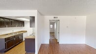Located at 10134 W Mohawk Ln in Peoria, Arizona, this single-story, one-bedroom, two-bathroom home offers a practical and comfortable layout. The open living room greets you at the entrance, featuring wood-look laminate flooring, bright white walls, and large windows fitted with blinds that invite natural light and views of the surrounding greenery. A textured ceiling adds character throughout the main living areas. The galley-style kitchen is a functional highlight, showcasing dark espresso cabinetry, granite-style countertops, a double basin sink, a skylight overhead, and white appliances including a range and refrigerator — all set atop matching wood-look flooring. The generously sized primary bedroom is carpeted for comfort and includes a ceiling fan, a textured ceiling, and direct access to a well-appointed en-suite bathroom featuring dark vanity cabinetry and granite-style counters. A second full bathroom serves the rest of the home, complete with a shower/tub combo equipped with grab bars, a large mirror, and matching granite-style countertops. A connecting hallway ties the layout together efficiently, making this home a well-organized and inviting space in the heart of Peoria, AZ.