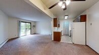 This single-floor unit offers a practical and comfortable layout that seamlessly connects the main living areas. The open-concept living and dining space is generously sized, finished with wall-to-wall carpet and neutral walls that create a bright, welcoming atmosphere. A sliding glass door leads to a private balcony, filling the room with natural light and providing views of the surrounding greenery. A wall-mounted air conditioning unit and baseboard heating ensure year-round comfort. The kitchen is positioned adjacent to the living area and features warm wood cabinetry, white countertops, a black coil-top electric range with a range hood, and a full-size refrigerator. A textured ceiling and functional overhead lighting complete the kitchen space. The bedroom is a well-proportioned room with plush carpet, a ceiling fan with light fixture, a wood-framed window overlooking lush outdoor greenery, and baseboard heating. The full bathroom is cleanly appointed with a single-sink vanity with wood cabinetry, a large mirror, white tile surround, and a combined tub and shower. Throughout the unit, a consistent use of neutral tones and practical finishes creates a cohesive and livable environment.