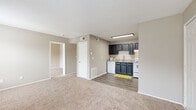 This single-floor residential unit offers a practical and comfortable layout designed for everyday living. The open-concept living area is finished with plush wall-to-wall carpeting and neutral warm-toned walls, creating a welcoming atmosphere. The space flows directly into the kitchen, which features dark navy cabinetry contrasted against light countertops, a stainless steel sink, a white electric range, and a dishwasher. Durable wood-look plank flooring grounds the kitchen area, adding visual contrast to the carpeted living space.

The bedroom is generously sized, bathed in natural light through dual windows, and equipped with a ceiling fan with light fixture. A second bedroom or additional room is also carpeted and includes its own window and ceiling fan. The primary bedroom connects directly to the bathroom area, which includes a wide vanity with dark cabinetry, a large mirror with lighted fixture, and access to a full bathroom complete with a tub and shower combination. Throughout, the unit maintains a clean, neutral palette with textured ceilings, white trim, and consistent finishes that provide a cohesive and functional living environment.