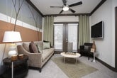 This single-floor residence offers a thoughtfully designed layout comprising multiple bedrooms, two full bathrooms, a functional kitchen, and a characterful living area. The kitchen features dark espresso cabinetry paired with granite countertops, tile flooring, and stainless steel appliances, creating a sleek, contemporary workspace. Two-panel interior doors finished in a warm taupe tone appear consistently throughout, lending a cohesive design aesthetic to the space.

The living area serves as a visual centerpiece, highlighted by a striking hand-painted tree mural accent wall in muted earth tones and blues, complemented by a ceiling fan and access to an outdoor area via glass-paneled doors. The bedrooms are carpeted and well-lit by large windows dressed with decorative curtains and blinds, each equipped with ceiling fans. One bedroom features a bold slate-blue accent wall, while others maintain neutral warm tones.

The primary bathroom includes a granite vanity, a glass-enclosed walk-in shower, and direct access to a walk-in closet. A secondary bathroom offers a granite vanity and a tub-shower combination. Together, the rooms reflect a consistent palette of dark wood trim, granite surfaces, and warm neutral tones throughout.