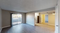 This single-floor residence offers a well-organized layout with distinct living, kitchen, sleeping, and bathroom areas connected by consistent laminate wood-style flooring. The open living room is bright and airy, featuring a textured ceiling, neutral gray walls, and a sliding glass door that leads to a private balcony with outdoor views — allowing natural light to fill the space. The galley-style kitchen is efficiently designed with white cabinetry, dark countertops, stainless steel appliances including a refrigerator and electric range, and a window that brings in additional natural light. A ceiling fan is installed in the secondary living area, which also features multiple doors providing access to additional rooms and storage. The bedroom is a well-proportioned, quiet retreat with laminate flooring, neutral tones, and a window offering natural light. The bathroom is clean and functional, complete with a tub-shower combination, a toilet, a vanity with dark countertop, and wood-style tile flooring. Throughout the unit, white trim work, neutral wall tones, and consistent flooring choices create a cohesive and modern aesthetic that is both practical and inviting.