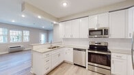 Located at 35 Violet Ave in Poughkeepsie, NY, this single-floor unit offers a thoughtfully designed layout with modern finishes throughout. The kitchen is a standout feature, showcasing crisp white shaker cabinetry, granite countertops, a subway tile backsplash, and a full suite of stainless steel appliances including a refrigerator, electric range, over-the-range microwave, and dishwasher. A double basin sink is positioned along the peninsula, providing both functionality and an open sightline into the adjacent living area. Light wood-look flooring runs seamlessly throughout the main living spaces, complementing the warm neutral wall tones and crisp white trim. The living area is generously proportioned, bathed in natural light through multiple windows, and equipped with a wall-mounted PTAC unit for climate control. A glass-paned exterior door offers convenient access to the outdoors. The bedroom spaces are well-sized with the same warm palette, ample natural light, and recessed LED lighting. The bathroom features elegant marble-look tile flooring, a white vanity with granite countertop, and a clean, minimalist design. Recessed lighting and a thermostat are also present, rounding out the unit's practical and polished appeal.