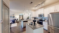 Located at 7201 Charlotte Pike in Nashville, Tennessee, this single-floor residence offers a well-designed open-concept layout that blends functionality with modern style. The kitchen is a standout feature, equipped with white shaker-style cabinetry, granite countertops, a subway tile backsplash, stainless steel appliances including an electric range, microwave, refrigerator, and dishwasher, plus a central island with additional granite workspace. Track lighting and pendant fixtures illuminate the kitchen, which flows seamlessly into the living area through an elegant arched doorway. The living space features warm wood-look flooring that carries throughout the main areas, creating a cohesive and inviting atmosphere. The bedrooms are generously sized, each featuring plush carpeting, windows with natural light and exterior views, and ample room for furnishings. Two full bathrooms feature granite-topped vanities, tile flooring, and full soaking tub and shower combinations with curved curtain rods. Additional highlights include in-unit laundry, a utility/storage area with closet doors, and a neutral color palette throughout that lends the space a clean, contemporary feel.