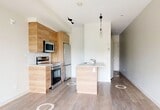 Located at 11329 University Avenue NW in Edmonton, Alberta, this efficiently designed unit is part of a contemporary multi-storey residential building featuring a modern exterior of wood cladding and grey panelling. The interior is bright and clean, with white walls and light-toned luxury vinyl plank flooring that contribute to an airy, minimal aesthetic throughout.

The kitchen is a standout feature, outfitted with warm wood-grain cabinetry extending to the upper walls, light stone-effect countertops, white subway tile backsplash, and a full suite of stainless steel appliances including a range with oven, over-the-range microwave, and refrigerator. The layout is thoughtfully arranged to maximize efficiency within the compact footprint.

The bathroom offers a clean, contemporary finish with a warm wood vanity, light stone countertop, undermount sink, chrome fixtures, a full-size soaker tub, and large-format white wall tiles. A wide mirror adds brightness to the space.

The hallway connects the rooms with clean lines and ample natural light visible from the entrance. The unit also features access to a private balcony with glass-panel railings, offering views of the surrounding tree-lined streetscape — an ideal outdoor extension of the living space.