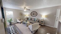 Located in Fort Worth, Texas, this well-appointed single-floor residence at 4858 River Ranch Blvd offers a cohesive and inviting interior defined by warm neutral tones, wood-look flooring, and tasteful decorative accents throughout. The living area serves as the heart of the home, featuring a ceiling fan, textured ceiling, and generous natural light filtering through vertical blinds. Comfortable seating, a mirrored glass coffee table, and decorative wall art create a welcoming and stylish atmosphere. A large bold canvas and sunburst wall medallions add personality to the space. The kitchen is thoughtfully designed with crisp white cabinetry, light countertops, a mosaic tile backsplash, and black appliances, including a dishwasher and range. Track lighting overhead ensures a bright and functional workspace. The bedroom is a serene retreat, with soft neutral walls, a textured ceiling, rich hardwood-style flooring, and a large window dressed with sheer curtains that allow natural light to filter in gently. A dedicated vanity nook adjacent to the bathroom offers an intimate space with tufted seating, abstract wall art, and a sleek console table. The bathroom features white cabinetry and a well-lit vanity mirror. Every detail of this home reflects a refined, contemporary sensibility.