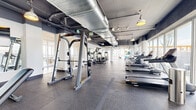 Located at 1625 NW 20th St in Miami, FL, this fitness center offers a generously sized, single-floor exercise space designed with both functionality and aesthetic appeal in mind. The facility showcases an industrial-chic design, with exposed ductwork and concrete ceilings painted in a bold dark tone, complemented by pendant-style industrial lighting that adds warmth and character throughout.

Floor-to-ceiling windows line the perimeter, flooding the space with abundant natural light and providing open views of the surrounding Miami cityscape. The durable rubber flooring underfoot provides both safety and comfort across the entire exercise area.

The cardio zone is well-equipped with multiple Spirit treadmills and elliptical machines, allowing for ample room between each unit. A dedicated strength training section features cable machines, a Smith machine, adjustable benches, a full dumbbell rack, and a weight plate storage system. Large wall mirrors are strategically positioned throughout the strength area to assist with form and enhance the sense of space.

A functional training zone with stability balls and additional accessories rounds out the facility's offerings. The open, airy layout ensures comfortable circulation throughout, making this fitness center a comprehensive and well-appointed destination for a full-body workout.
