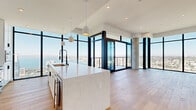 Located in the heart of San Diego at 1401 Union St, this high-rise residence offers a striking blend of contemporary design and sweeping panoramic views of San Diego Bay and the surrounding cityscape. Floor-to-ceiling windows with sleek black frames flood the open living areas with natural light, while wide-plank hardwood flooring runs throughout, adding warmth to the modern aesthetic. The living area features a built-in fireplace and an exposed concrete column, lending an industrial-chic character to the space. A private balcony extends the living area outdoors, offering unobstructed views of the bay and skyline. The gourmet kitchen is appointed with a generous waterfall-edge marble island, white shaker cabinetry, premium stainless steel appliances, and pendant lighting — all framed by spectacular water views. The primary bathroom is finished with large-format neutral tiles, a glass-enclosed walk-in shower, a soaking tub, dual vanities with matte black fixtures, and illuminated mirrors. A custom walk-in closet features rich wood built-ins with integrated lighting, generous shelving, and dedicated drawer storage. An in-unit laundry area adds everyday convenience. Throughout, clean lines, high-end finishes, and abundant natural light define the refined, elevated living experience this residence delivers.
