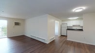 This single-floor, 2-bedroom, 2-bathroom unit offers a clean and functional layout designed for comfortable everyday living. The open living area is finished with rich, dark hardwood-style flooring that extends throughout the main living space and into the kitchen, creating a cohesive and polished look. The kitchen is well-appointed with white shaker-style cabinetry, dark countertops, a tiled backsplash, and a full suite of white appliances including a refrigerator, electric range, built-in microwave, and dishwasher. A pass-through counter connects the kitchen to the living area, enhancing the open feel of the space. Both bedrooms are carpeted for comfort and feature ceiling fans with light fixtures. One bedroom benefits from a window that brings in natural light, while the other offers direct access to the main hallway. Each bathroom is finished with wood-style flooring, white tile walls, and a clean, bright aesthetic. One bathroom includes a full tub-shower combination with subway tile surround, while the other is accessed through louvered bi-fold doors. Built-in closet storage and baseboard heating are present throughout, rounding out this practical and well-maintained unit.