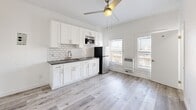 Located at 744 Beacon Avenue in Los Angeles, CA, this efficiently designed single-floor unit offers a clean, modern aesthetic with a bright and airy feel. The interior is finished with light gray wood-look flooring throughout the main living areas, contrasting with white tile in the bathroom, creating a cohesive and contemporary look.

The kitchen is a standout feature, outfitted with crisp white shaker cabinets, dark countertops, a subway tile backsplash, a stainless steel sink, a built-in microwave, and a full-size refrigerator. A ceiling fan with a light fixture keeps the space comfortable, while large windows allow ample natural light to pour in, enhancing the open feel of the kitchen and living area.

The living space is open and versatile, with clean white walls, high baseboards, and a ceiling fan that adds both function and style. A wall-mounted heater unit provides climate control. Natural light flows through multiple windows fitted with blinds, contributing to the bright, welcoming ambiance.

The bathroom is accessed through a dedicated doorway and features light tile flooring and walls, maintaining the clean and minimal design language of the rest of the unit. A secondary entry door provides convenient access. Overall, this space presents a well-appointed, move-in-ready layout ideal for efficient urban living in the heart of Los Angeles.