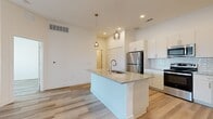 This thoughtfully designed 1-bedroom, 1-bathroom unit offers a clean, modern aesthetic with light wood-style flooring and crisp white walls carried consistently throughout the space. The open-concept kitchen is a standout feature, anchored by a central island with a granite countertop, undermount sink, and stylish pendant lighting overhead. White shaker cabinetry, a decorative tile backsplash, and a full suite of stainless steel appliances — including a refrigerator, range, and microwave — complete the kitchen. The adjoining living area is bright and open, providing a versatile layout suited for a variety of furniture arrangements. The bedroom is a comfortable, well-proportioned retreat featuring a ceiling fan, a large window with outdoor views of surrounding greenery, and a private door leading to a balcony. Direct access to the bathroom and a dedicated closet add convenience. The bathroom is finished with granite countertops matching the kitchen, light wood cabinetry with modern hardware, a large vanity mirror, and built-in shelving. The closet provides organized storage space. Recessed lighting and clean white finishes throughout give the entire unit a bright, contemporary feel.