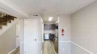 This two-floor unit is designed with a clean, contemporary aesthetic, utilizing a neutral gray and white color palette that creates a bright, cohesive atmosphere throughout. Light-toned, wood-style luxury vinyl plank flooring runs through the main living and kitchen areas, while plush carpeting covers the bedroom spaces, adding warmth and comfort.

The kitchen is a functional highlight, equipped with gray shaker-style cabinetry, white countertops, and a full suite of stainless steel appliances including a gas range, built-in microwave, dishwasher, and refrigerator. A skylight overhead supplements the overhead lighting, keeping the space well-lit. White wainscoting in the hallway leading to the kitchen adds a structured, polished detail.

The living area features large sliding doors with vertical blinds, allowing ample natural light and outdoor views. Multiple additional rooms — suitable for bedrooms or flex spaces — feature carpeted or vinyl plank flooring and windows with horizontal blinds that invite natural light. The bathroom includes a full tub and shower combination with white tile surround and chrome fixtures.

Overall, the unit presents a well-maintained, move-in ready interior with consistent finishes across both floors, offering a practical and comfortable living environment.