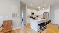 This contemporary 820 square foot apartment offers a thoughtfully designed living space with two bedrooms and two bathrooms. The heart of the home is an open-concept living area, seamlessly connecting the kitchen, dining, and living spaces. The kitchen boasts crisp white cabinetry, stainless steel appliances, and a functional island with seating, perfect for casual dining or entertaining.

Natural light floods the space through large windows, enhancing the airy feel of the home. The living room features a comfortable gray sofa, accented with colorful pillows, and unique oval mirrors that add depth to the space. Hardwood floors run throughout, lending warmth and continuity.

The primary bedroom, measuring 140 square feet, is a serene retreat with a large window offering outdoor views. Both bedrooms are well-appointed with modern furnishings and ample natural light. The bathrooms are stylishly designed with clean lines and contemporary fixtures.

Thoughtful details like pendant lighting, artistic wall decor, and strategically placed plants contribute to the overall modern aesthetic. The apartment also offers outdoor access, likely through a balcony or patio, extending the living space and providing a connection to the surrounding environment.