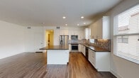 Located at 10858 Telegraph Rd in Ventura, California, this well-appointed single-story unit offers a thoughtfully designed layout with modern finishes throughout. The heart of the home is a spacious, open-concept kitchen featuring crisp white shaker cabinetry, dark quartz countertops, a mosaic tile backsplash, and a full suite of stainless steel appliances including a French door refrigerator, gas range, built-in microwave, and dishwasher. A central island provides additional prep space and casual seating, while recessed lighting and under-cabinet lights enhance the bright, functional atmosphere. The kitchen flows seamlessly into a generous living area finished with rich hardwood-style flooring that extends throughout the unit. Large windows fitted with blinds invite abundant natural light and offer views of the surrounding neighborhood. The bedroom features mirrored sliding closet doors and multiple windows, creating an airy, well-lit retreat. The bathroom is finished with a white vanity, dark countertop, chrome fixtures, and a large mirror, maintaining the clean, contemporary aesthetic found throughout. A dedicated in-unit laundry room accommodates a full-size side-by-side washer and dryer alongside a tankless water heater and additional cabinetry for storage.