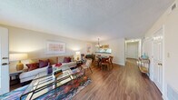 This two-story residence offers a well-organized layout spread across two evenly sized floors. The main level features an open-concept living and dining area unified by warm hardwood-style flooring and a textured ceiling. The living room receives natural light through a glass-paneled patio door with plantation shutters, providing direct outdoor access. A dedicated seating nook adds a cozy retreat within the living space.

The dining area is anchored by a classic chandelier and connects directly to the kitchen via a pass-through window — a practical design detail that enhances the flow between spaces. The kitchen features warm oak cabinetry, dark granite-style countertops, and hardwood-style flooring, offering ample storage and workspace.

Upstairs, the primary bedroom is a comfortably sized retreat with plush carpeting, a natural window view, and a double-door closet alongside an additional door for storage or ensuite access. The second bedroom is equally functional. Both bathrooms include vanities with dark countertops and full tub-shower combinations. A hallway connects the upper-level rooms, completing this efficiently designed two-floor home.
